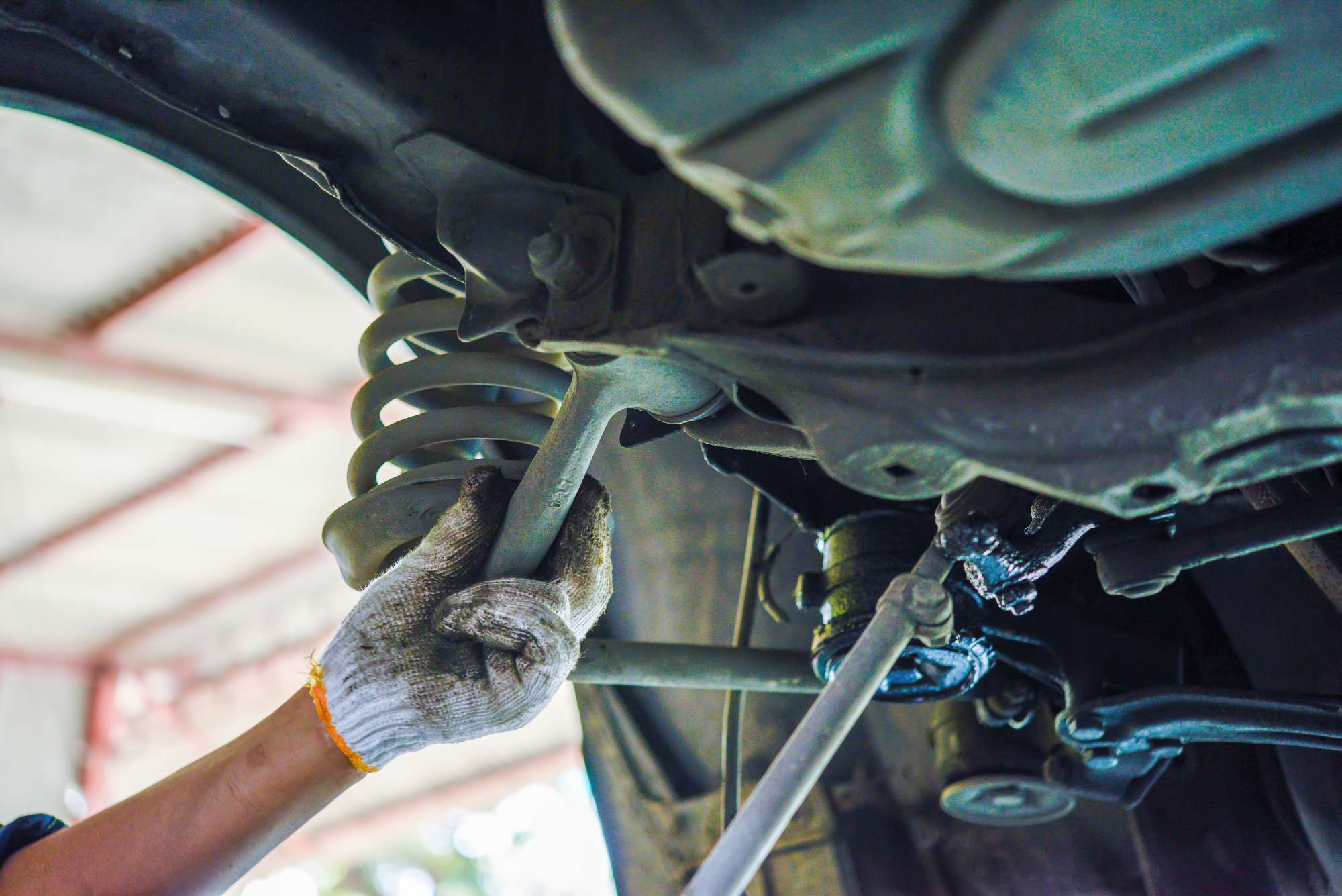 自動車整備士が車両下部のサスペンション部品を修理している作業