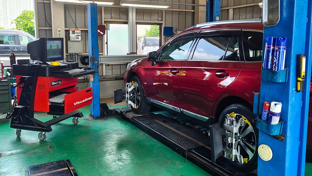 赤い車が自動車整備工場でホイールアライメントの検査をしている