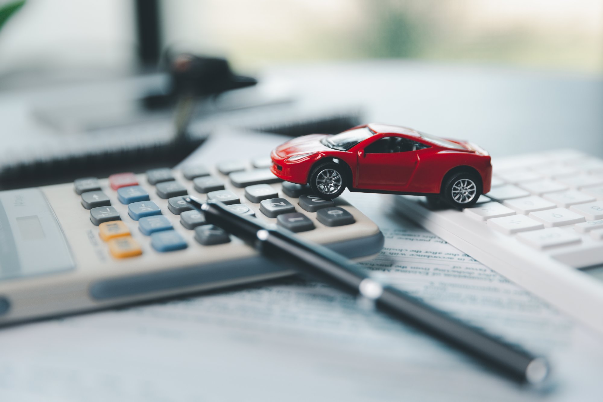 電卓の上に置かれた赤いミニチュア車と見積書