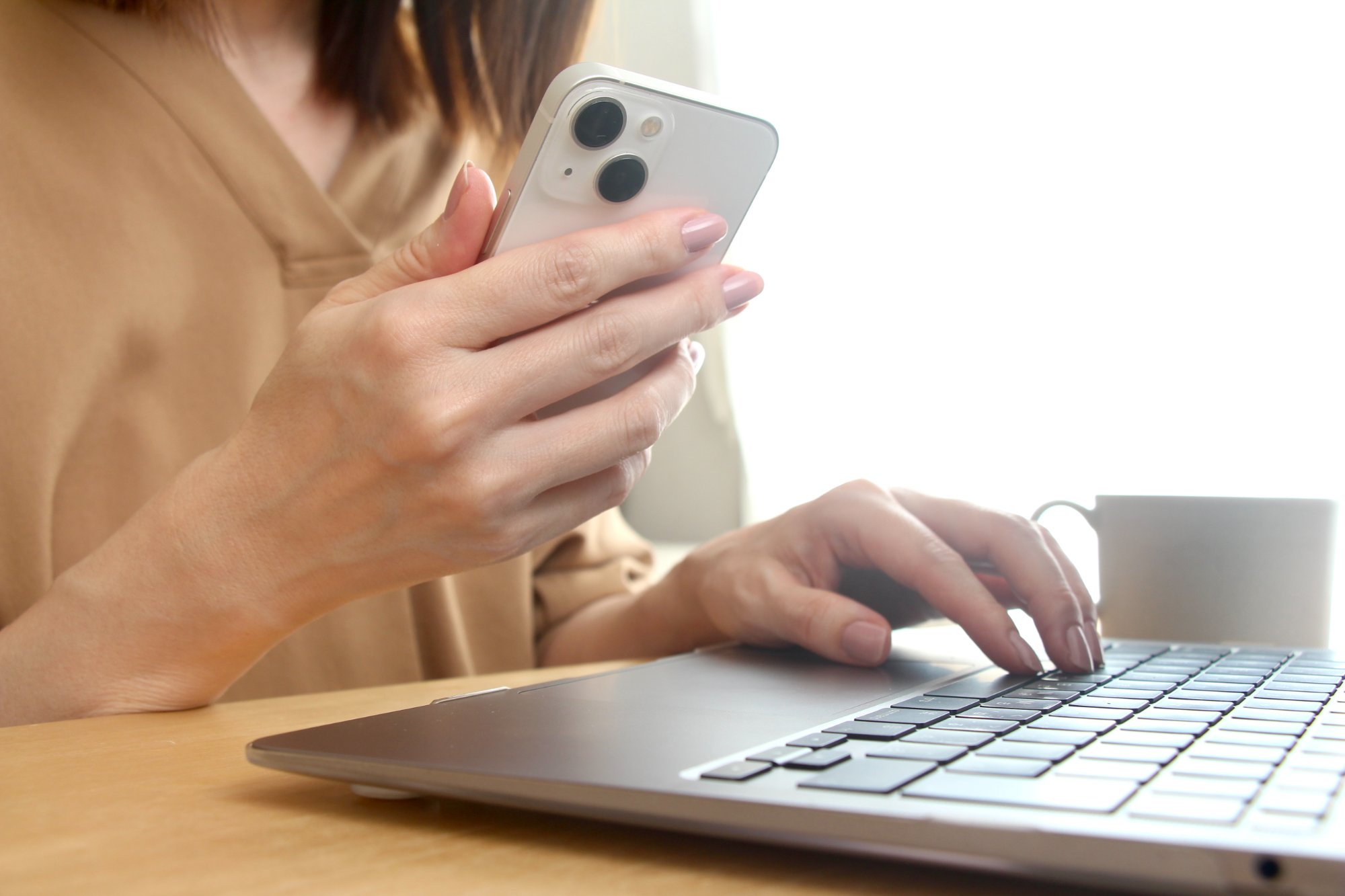 ノートパソコンとスマートフォンを同時に使用する女性の手元