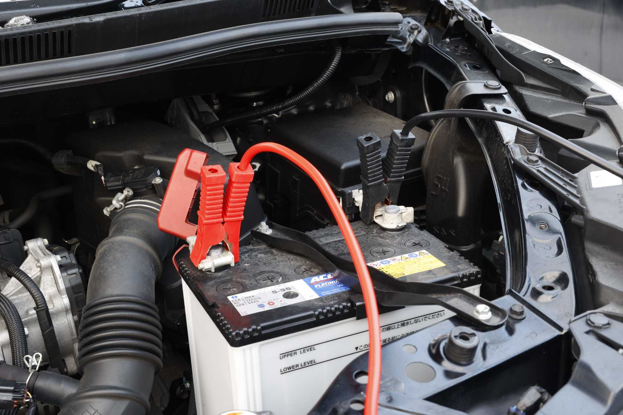 赤いジャンプケーブルが接続された車のバッテリー交換作業